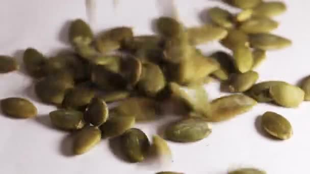 Крупный план падения очищенного семян тыквы и вращения на белом столе — стоковое видео