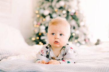 Çocuğun ilk Noel 'i. Dalgın üzgün küçük bir çocuk, parlak dekore edilmiş çelenkli bir köknar ağacının arka planında şenlikli bir kostümle yatıyordu. Noel konsepti..