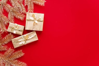 Kırmızı Noel ya da yeni yıl geçmişi, altın Noel hediyelerinin ve altın köknar dallarının sade kompozisyonu, düzlük, düzlük, mesajlaşma için boş alan. Noel konsepti..