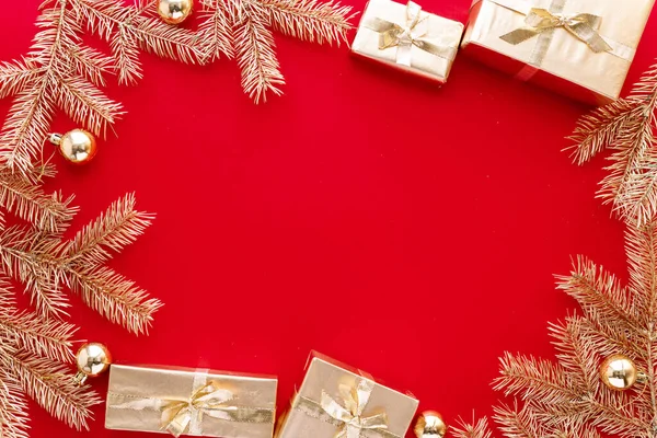 Roter Weihnachts- oder Neujahrshintergrund, schlichte Komposition aus goldenen Weihnachtsgeschenken und goldenen Tannenzweigen mit Weihnachtsspielzeug, Flatlay, leerer Raum für Grußtexte.. — Stockfoto