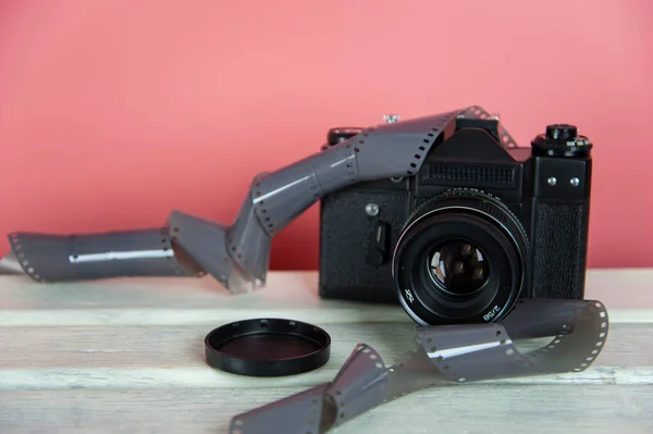 camera and photo film on a white surface with a pink background