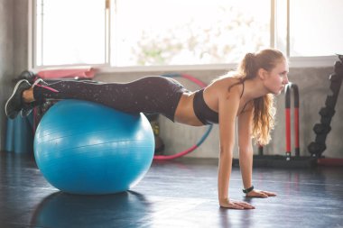 Genç ve güzel bir kadın spor salonunda topa uygun pilates egzersizleri yapıyor..