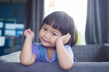 Sevimli küçük kız kanepede elleri çenesinde yatıyor ve evdeki televizyon ekranının ışığında sıkılıyor..