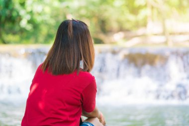 Kök ağacında oturan ve şelale manzarasının tadını çıkaran genç bir kadın. Chet Sao Noi Şelalesi Ulusal Parkı 'nda güzel bir şelalenin yanında doğa gezintisi.