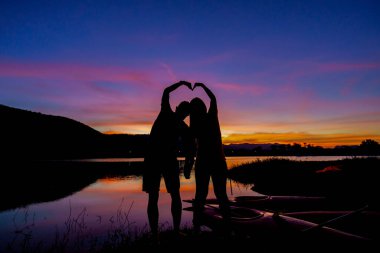 Gün batımında göl veya nehirde ellerinde kalp sembolü olan sevgili çift, özgürlük kavramını seviyor..