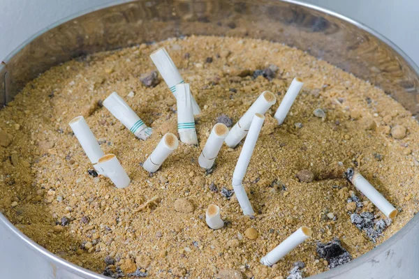 Cigarrillos ahumados en cenicero sucio con arena . — Foto de Stock