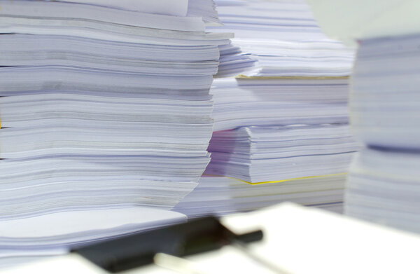 Pile of documents on desk stack up high waiting to be managed