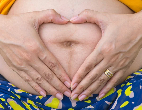 Wanita hamil dengan tangan dalam bentuk hati. — Stok Foto