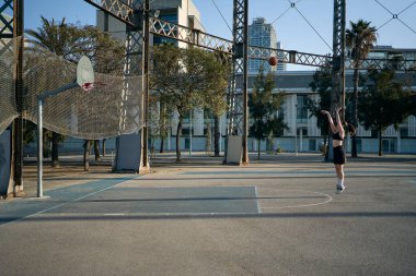 Sabahın erken saatlerinde basket sahasında üç sayı çizgisinden ateş eden bir kızın genel çekimi..