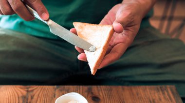 Ekmeğe tereyağı süren bir adam. Tavuklu kızarmış yumurta.