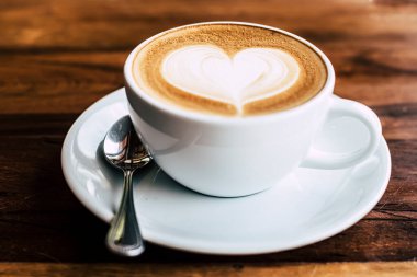 Sabah güneş ışığı altında, eski ahşap arka planda kalp şeklinde bir fincan kahve.