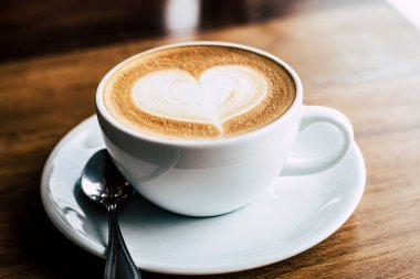 Sabah güneş ışığı altında, eski ahşap arka planda kalp şeklinde bir fincan kahve.