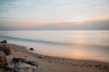 Uzun pozlu deniz kayaları güneşin doğuşunda muhteşem gündoğumu manzarası huzur dolu bir sabah denizinde romantik atmosfer. Pembe ufuk ve ilk sıcak güneş ışınları.