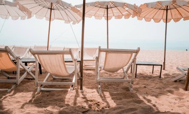 Güverte sandalyeleri ve tropik plajda beyaz şempanzeler. Yazın kumsalda beyaz şemsiye