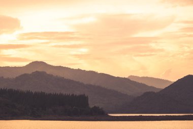 Güneş doğarken ağaçlarla kaplı, dağların sisli katmanlarının dramatik manzarası. Ormandaki dağ yamacında sisli renkli gündoğumu