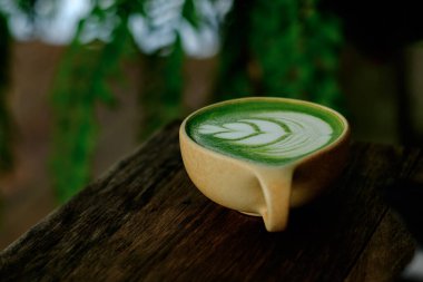 Kırsal ahşap bir yüzeyde durmakta olan yumuşak yapraklı, bir fincan kibritli latte. Topraksı kahverengi ve doğal yeşil tonlar sıcaklığı, sadeliği ve sakin farkındalığı çağrıştırıyor. Bu görüntü dengeyi, durgunluğu ve doğa ile uyumu sembolize eder.