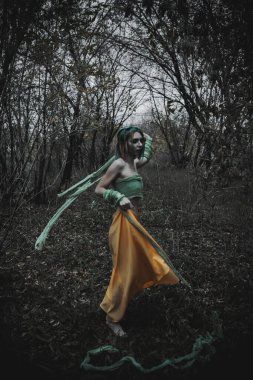Sonbahar yeşili içinde yeşil ve sarı cüppeli ölü bir kız.