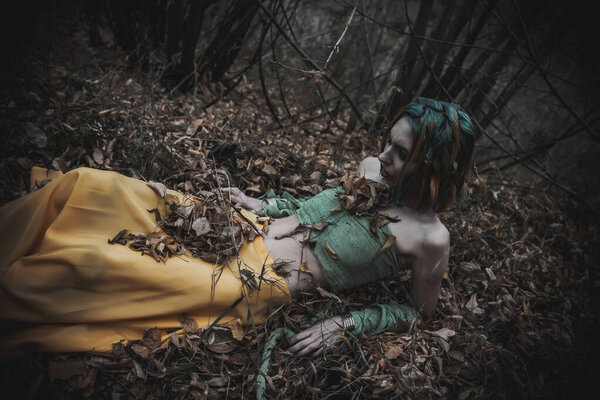 Dead girl in autumn foliage wearing green and yellow robes