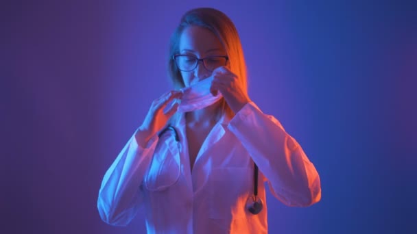 Красива жінка-лікар в окулярах і біле пальто надягає медичну маску на рот — стокове відео