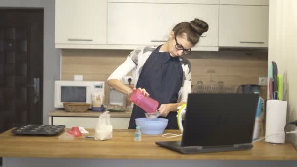 Beautiful young woman cooking with help of recipe on laptop — Stock Video