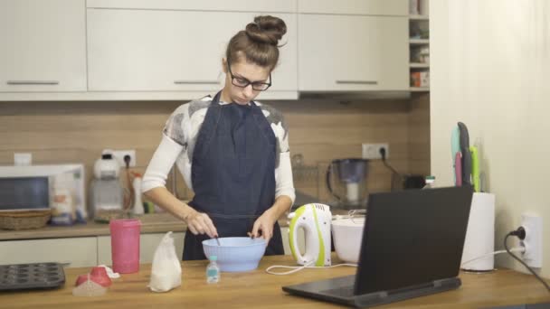 Woman cooking muffins whilst looking the recipe at laptop in the kitchen at home — Stock Video