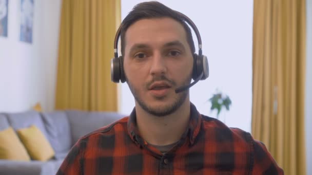Potret pemuda dengan headset nirkabel berbicara dengan pelanggan pada panggilan video — Stok Video