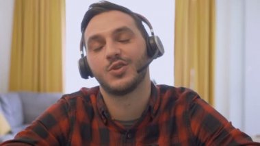 Kablosuz kulaklık takmış yakışıklı bir gencin video görüntüsü. Kameranın önünde oturup müşteriyle görüntülü konuşma.