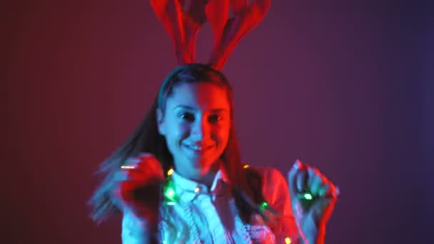 Baile de navidad mujeres atractivas en luces de neón y cuernos de ciervo — Vídeos de Stock