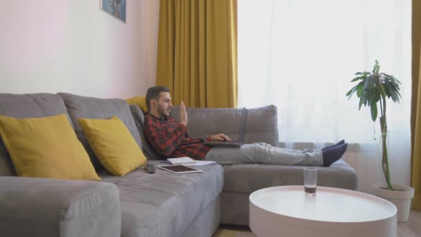 Um jovem que trabalha em casa começa a falar enquanto faz uma videochamada — Vídeo de Stock