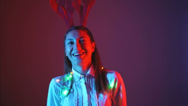 Jolie jeune femme avec des lumières de Noël et des bois de renne dansant — Video