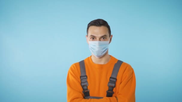 Endüstriyel iş kıyafetleri ve yüz maskesi takan ciddi görünüşlü bir adam elleri göğsünde kameraya doğru yürüyor. — Stok video