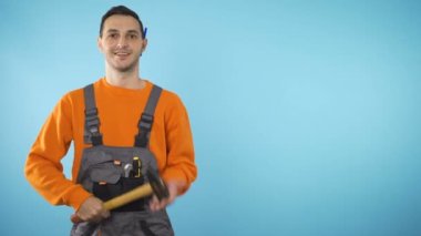 Gülümseyen inşaat işçisi elinde çekiç tutuyor, yardıma hazır.