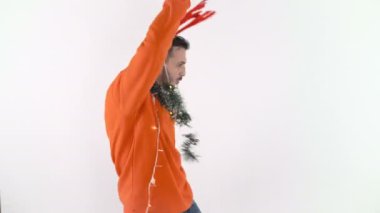Geyik boynuzları, çelenk ve Noel ışıkları olan genç adam dans ediyor ve gülümsüyor.