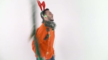 Yeşil bir çelenk sallayan ve dans eden genç ve mutlu bir adam. Kırmızı ren geyiği boynuzlarıyla Noel havasında bir adam.