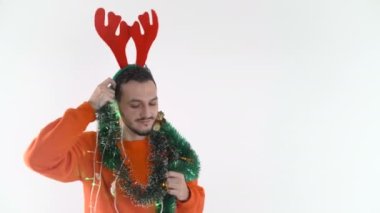 Geyik boynuzları ve Noel ışıkları olan dans edip şarkı söyleyen genç bir adam.