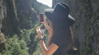 Siyah şapkalı kadın kaşifin arka planda güzel manzaralı akıllı telefonlu selfie çekişi.