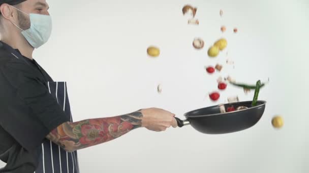 头戴面罩的纹身厨师把蔬菜放在白底平底锅里 — 图库视频影像