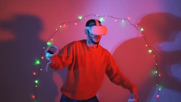 Fiatal férfi harcol a virtuális valóság segítségével swrods karácsonyi fények a háttérben — Stock videók