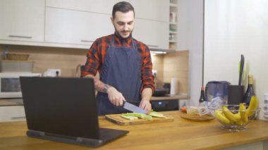 Önlüklü genç adam kilitlenirken evde yemek yapmayı öğreniyor.