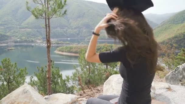 Ung kvinna sitter på bänken tittar på vacker sjö och fixa sin hatt — Stockvideo
