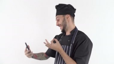 Mutlu, gülümseyen erkek aşçı akıllı telefonuyla konuşuyor ve heyecanlı bir şeyi açıklıyor.
