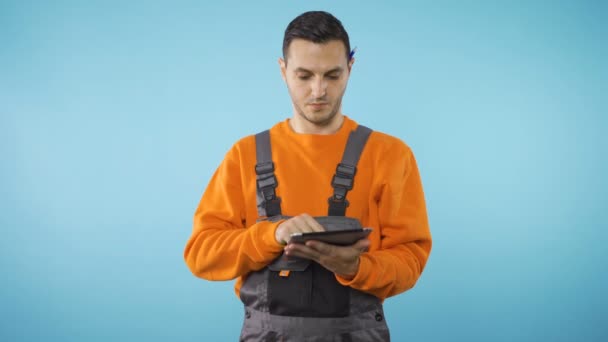 Arbeiter in industrieller Arbeitskleidung schaut sich um und schreibt auf Tablet — Stockvideo