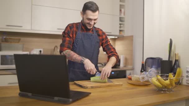 Jongeman in schort snijden groenten en het doen van video call op laptop — Stockvideo