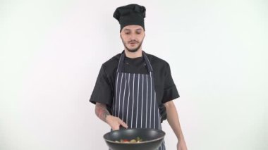 Gülümseyen adam kameranın önünde tavaya sebze atıyor.