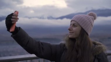Yüksek binaların balkonunda selfie çeken bir kadın.