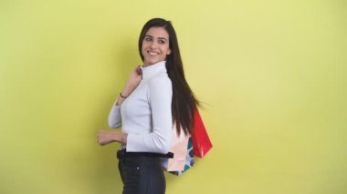 Gülümseyen genç bir kadın alışveriş torbaları taşıyor ve saçlarını sallıyor.