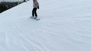 Dişi snowboardcu, dağ yamacına düşen kayak yamacından sağa sola dönüyor.