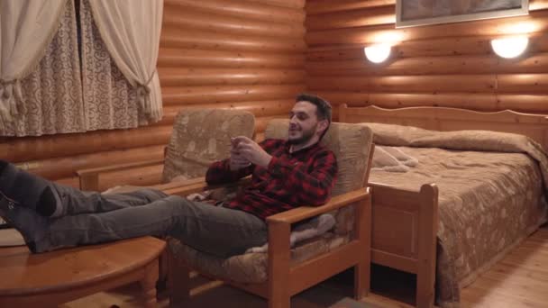 Man sitting on couch with feet up using his smartphone in wooden cabin — Stock Video