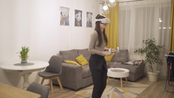 Счастливая молодая женщина с гарнитурой виртуальной реальности играет в игры и борется с помощью VR контроллеров — стоковое видео