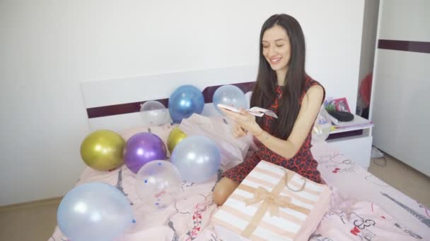 Gelukkig lachende vrouw met cadeaubon en zittend op bed met ballonnen en confetti — Stockvideo